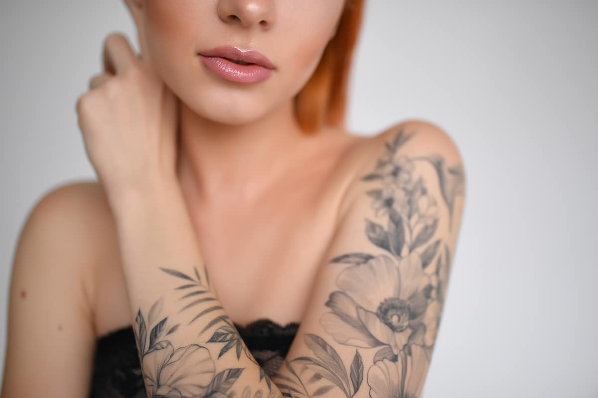 Beautiful girl with red hair in a lace black top on a white background. Tattoo with flowers and birds on hand. Nude makeup. Makeup model