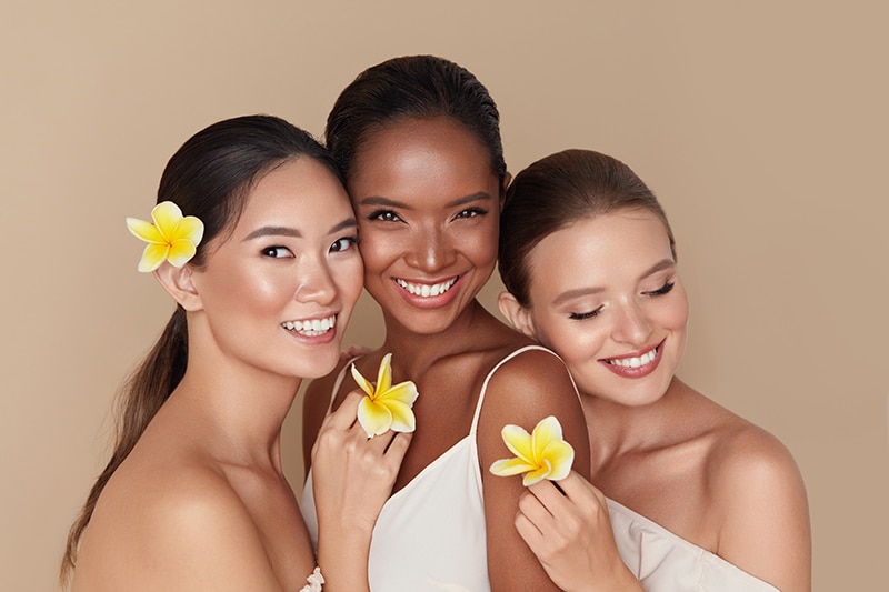 Diversity. Natural Beauty Portrait. Multi-Ethnic Women With Tropical Flowers Standing Together. Asian, Mixed Race And Caucasian Models With Nude Makeup And Healthy Skin Holding Plumeria.