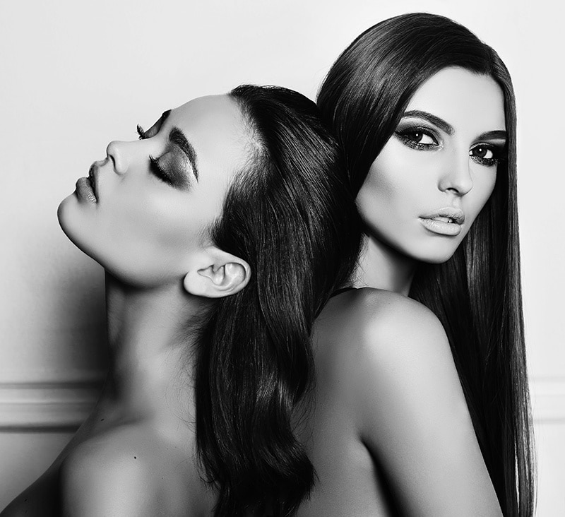 fashion black and white photo of two beautiful girls with dark hair and evening makeup, posing in studio