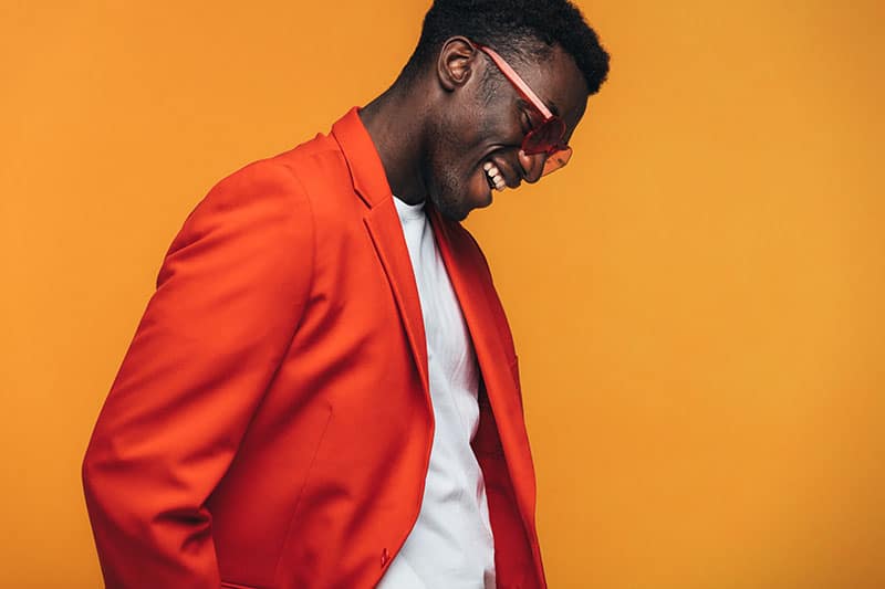 Handsome african male fashion model with sunglasses smiling against orange background. Stylish african man smiling in studio.